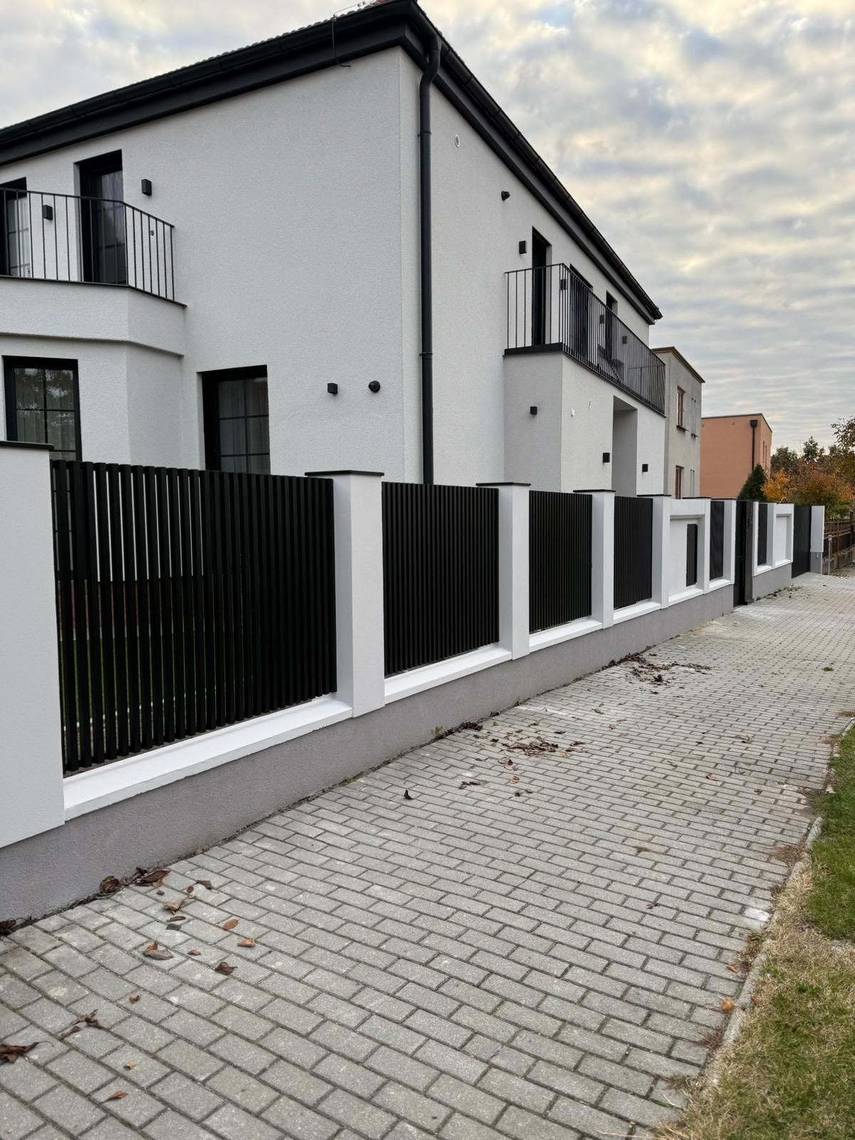 Řada černých lamelových výplní osazených mezi bílými zděnými sloupky