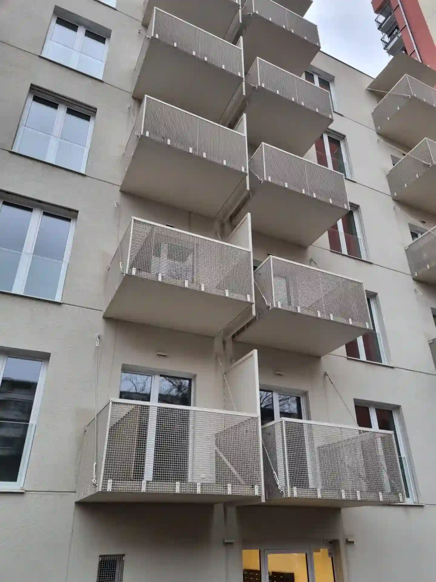 Přední fasáda bytového domu se závěsnými balkóny a lanovými záclon